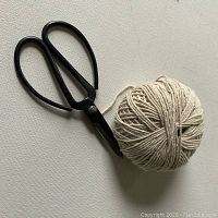 Black iron vintage style bonsai garden scissors resting next to a tightly wound ball of natural beige string on a white surface.