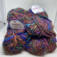 Eight multicolored skeins of Scheepjeswol Flamme Fine yarn showing the tightly packed skeins with colorful strand variations.