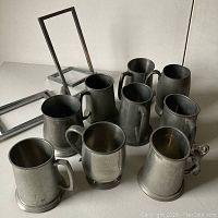 Collection display of eight pewter mugs and two aluminum picture stands on a flat surface