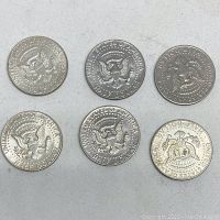 Six American Kennedy Half Dollar coins, reverse side showing the presidential eagle seal and "HALF DOLLAR" text, dated 1964, 1968, 1972 (two coins), and 1974 (two coins).