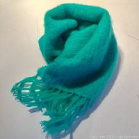 Green turquoise mohair and wool scarf folded showing fringe tassels on one end.