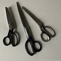 Three pairs of scissors including black handled scissors, one pair with serrated blades for pinking, viewed from above on a flat surface.