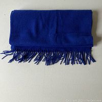 Folded blue wool scarf with fringed edges laid on flat surface.