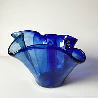 Side angle of deep blue Murano glass vessel showing wavy, folded rim and smooth glass body.