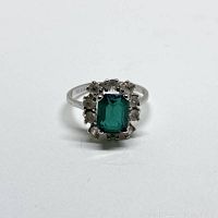 Front view of silver ring showing rectangular green glass center stone surrounded by clear simulated diamond stones in halo style setting.