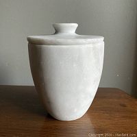 Front view of the Carrara marble jar with lid on, showing the overall shape, texture, and slight grey veining.