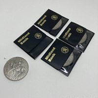 Four 1977 Queen Elizabeth II Silver Jubilee coins with black Midland Bank protective sleeves, arranged with one coin out of sleeve showing obverse horse and rider side.