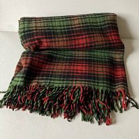 Folded green, red, and black plaid wool vintage blanket with fringed edges.