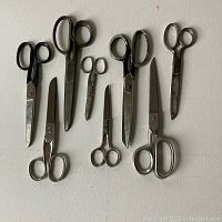 Eight pairs of vintage metal scissors arranged on white surface showcasing different sizes and handle shapes.
