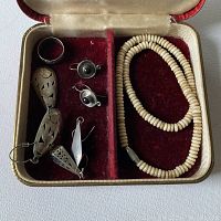 Open red faux leather jewelry box with velvet interior showing silver earrings, ring, and puka shell necklace inside