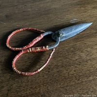 Close-up of antique hand-forged steel scissors with red and natural rattan wrapped handles on a dark wood surface