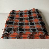 Folded vintage fabric showing orange, black, and brownish circular dots on grey background.
