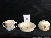 Three-piece Royal Doulton Bunnykins Shining Stars set: bowl, double handled cup, and piggy bank grouped against black backdrop