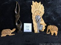 Full view of four wooden carvings on black surface, showing two animals, abstract sculpture, and face carving with leaf motif