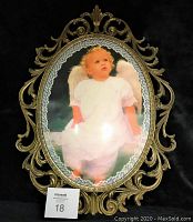 Photo of vintage brass metal oval frame with detailed scrollwork and decorative top, holding an image of a child dressed as an angel.