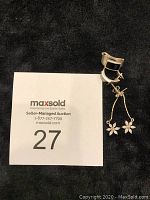 Two pairs of silver earrings together on black textured surface, one pair hinged hoops, one pair with flower dangles