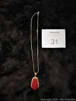 Full view of pendant necklace laid flat on black surface with lot number card nearby.