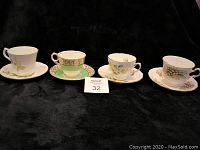 Four vintage bone china teacups and saucers displayed on black cloth, showing varied floral and decorative patterns.