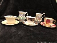 Front view of four vintage bone china teacups and saucers showing different patterns and designs including cream floral, tartan plaid with floral accents, lavender field, and red and gold striped.