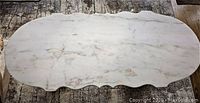Top view of oval white marble tabletop with grey veining and scalloped edges on textured rug