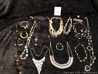 Full spread of assorted costume jewelry including necklaces, bracelets, earrings on black fabric.