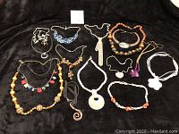 Full view of all necklaces laid out on black cloth background showing variety of materials, bead sizes, and pendant styles.