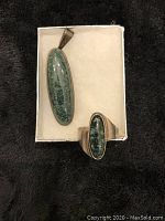 Silver pendant and ring with green elongated oval amazonite stones displayed on a white box and black background.