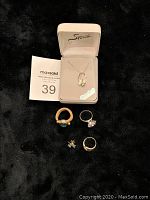 Lot of jewelry items shown on black fabric background including necklace in box, rings and earrings with MaxSold lot card.