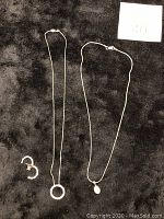 Photo showing two silver necklaces and one pair of silver crescent-shaped earrings grouped with maxsold number card.