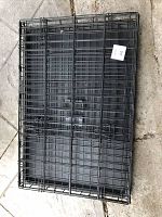 Folded flat black metal wire dog kennel with removable plastic tray, showing collapsed state for storage or transport.