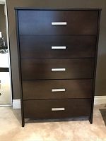 Front view of dark brown wooden vertical chest with 5 drawers and silver handles.