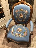 Front view of vintage Victorian style needlepoint armchair showing carved wood frame and detailed floral upholstery.