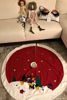 Two handmade rag dolls and a decorative dog face cushion arranged on a beige couch with the Christmas tree skirt laid out below.