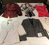 Six women's tops laid out on a bed to show variety and condition. Includes jackets and blouses in various colors and prints, all size M.