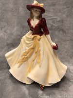 Front view of Royal Worcester porcelain figurine showing lady in red blouse, cream skirt with yellow sash, and red hat.