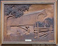 Full view of the vintage carved wooden art panel showing the detailed scene with a covered bridge, two figures by the water, tree, fence, and artist signature.