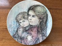Front view of the round decorative plate showing a painted image of a woman holding a child.