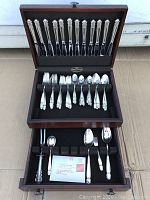 Full shot of open wooden box revealing the complete flatware set including knives, forks, spoons, and specialty pieces all neatly arranged in fitted slots within a black velvet-lined box.