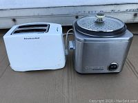 Photo showing the KitchenAid white toaster and stainless steel Cuisinart rice cooker/steamer side by side on a surface.