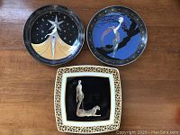 Three decorative plates displayed together: two round Royal Doulton House of Erte plates and one square Wild Cats Italian Ceramics Company plate.