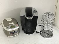 Keurig coffee maker, Zojirushi rice cooker, and coffee pod rack together on a white surface
