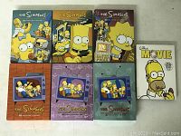 Overview photo of six seasons of The Simpsons TV show DVD sets plus The Simpsons Movie DVD case, all with illustrated covers featuring the Simpson family.