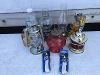 Overview of seven oil lamps and two packs of new oil lamp wicks, showing different lamp styles and chimneys.