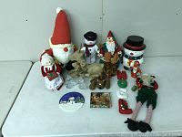 Overview of whole lot showing various Santa, snowman, reindeer figures and holiday ornaments on white table