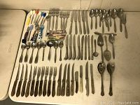 Overall assortment of silverware pieces laid out, showing different sizes and handle materials including plastic, wood-like, and metal handles.
