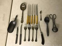 Full layout of all vintage kitchen utensils including knives, forks, spoons, scissors, and scoops arranged on flat surface.