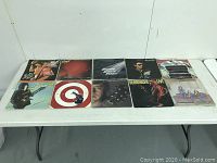 Photo showing 10 vinyl LP records laid out on a table. Albums include classic rock artists and bands with varied cover art styles and visible wear on sleeves.