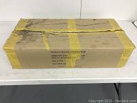 Closed cardboard box with yellow tape labeled Radisson Boston Production with product info and quantity 4.