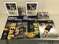 Various Boston sports memorabilia laid out on table including framed photos, banners, posters, and stack of magazines