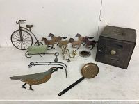 Photo showing entire lot including vintage metal warming oven, four horse figurines, metal bird, two carts, ladle, tongs, bicycle figurine and decorative plate.